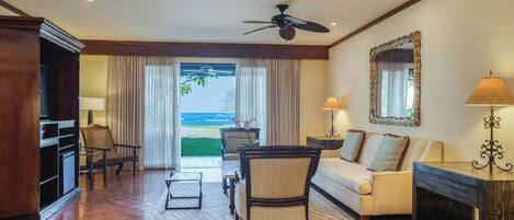 A spacious living area with a view of the ocean, a ceiling fan, a sofa, a coffee table, and a fireplace.