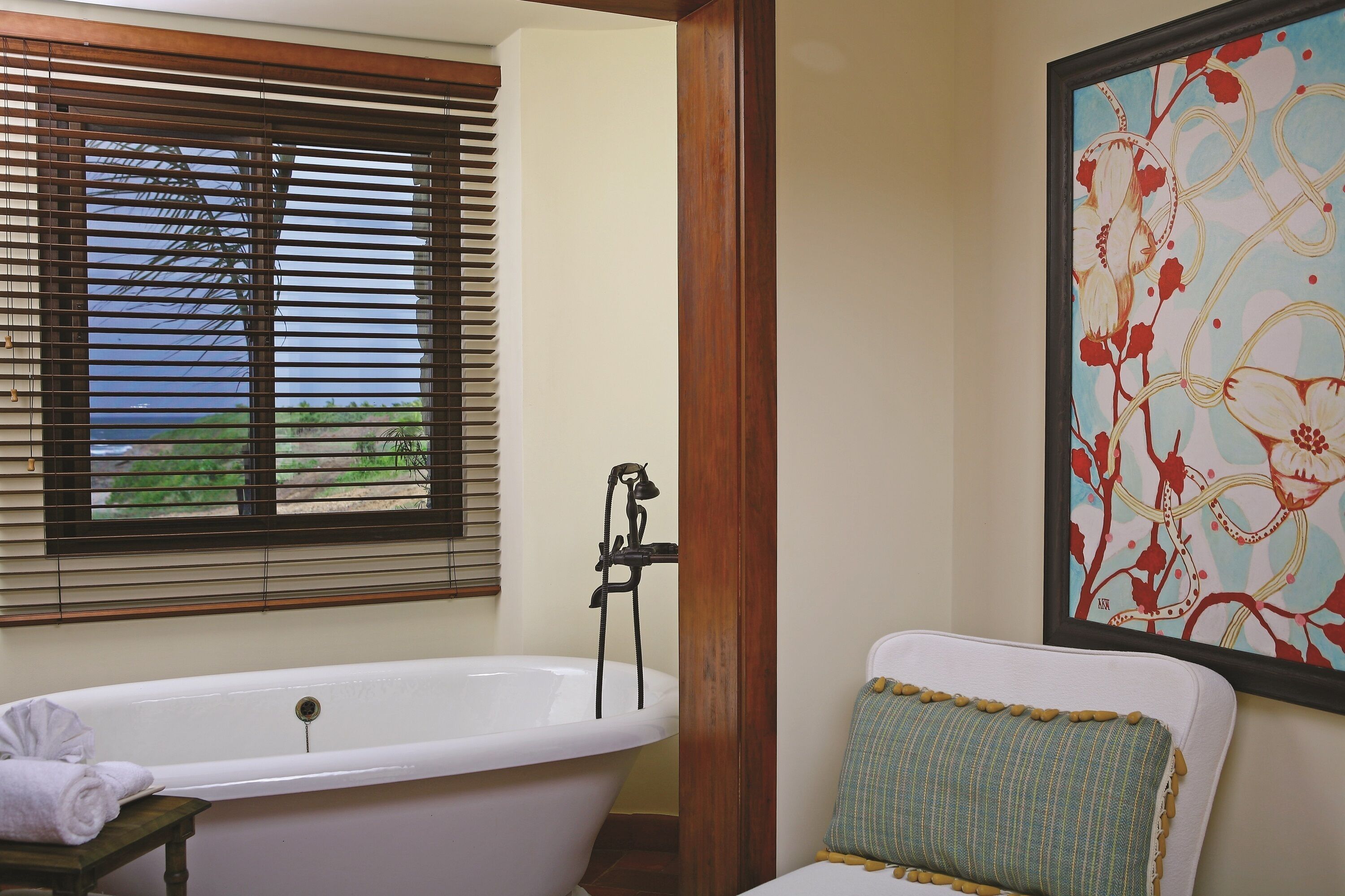 Un baño con bañera, ventana con persianas y un cuadro de flores en la pared.