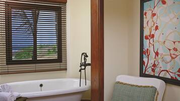 Un baño con bañera, ventana con persianas y un cuadro de flores en la pared.