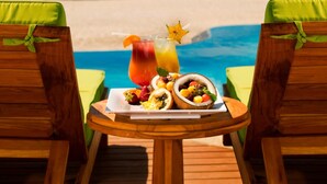A wooden deck with two green cushioned chairs facing a beach with a table in the center holding a fruit platter, a pitcher of juice, and a star-shaped decoration. - JW Marriott Guanacaste Resort & Spa (Tamarindo)
