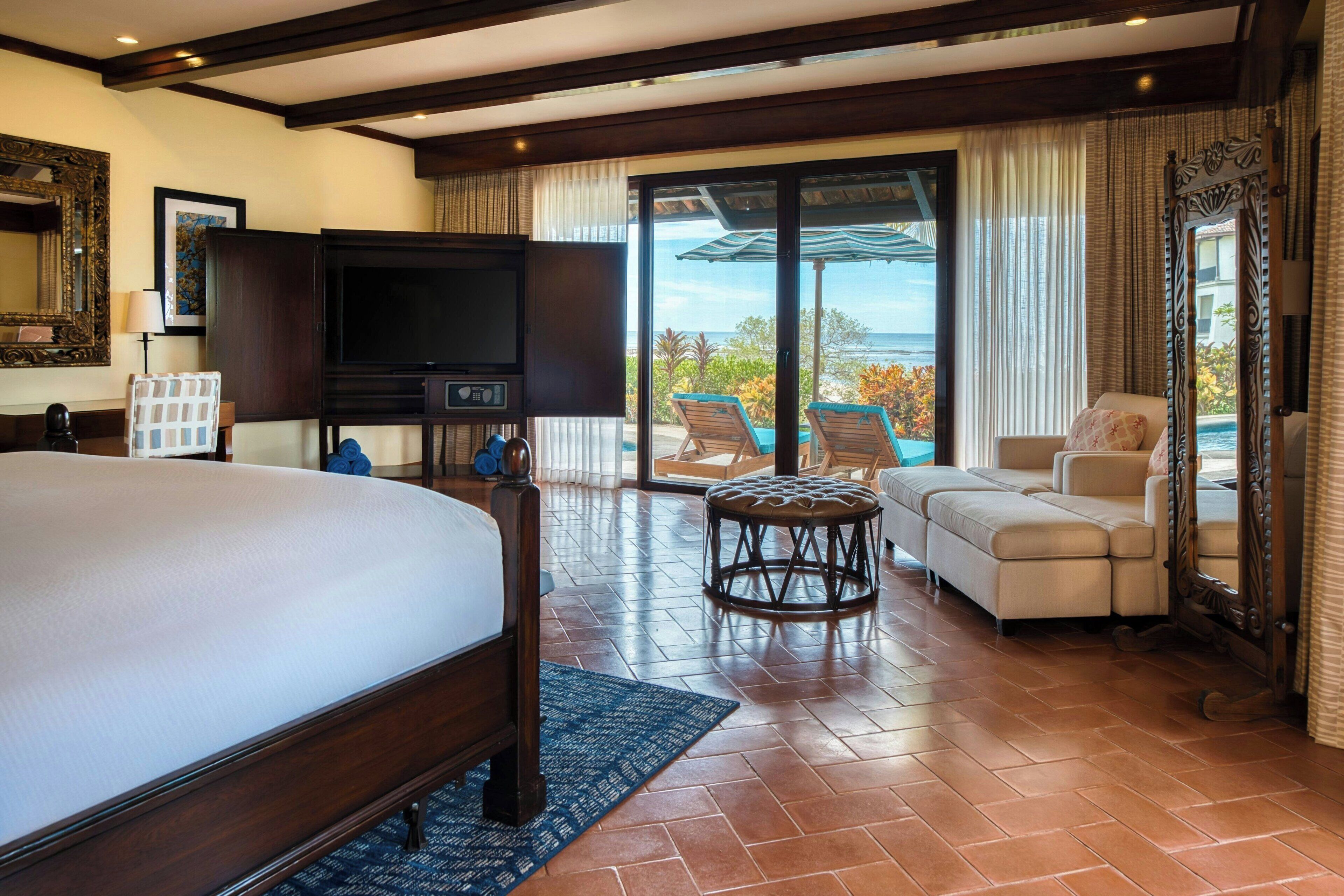 A hotel room with a large bed, a television, a sofa, and a view of the ocean.