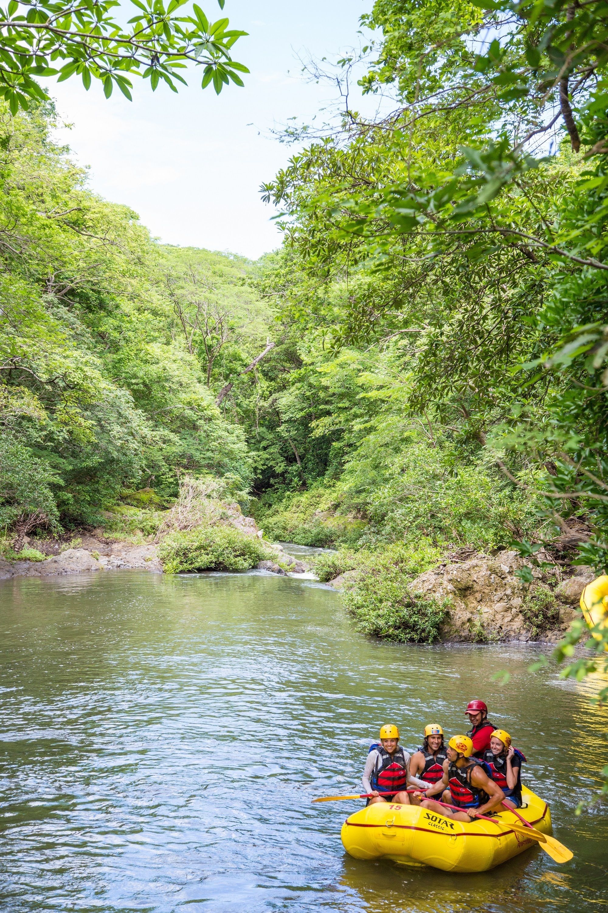 A group of people in a yellow raft on a river surrounded by dense greenery.