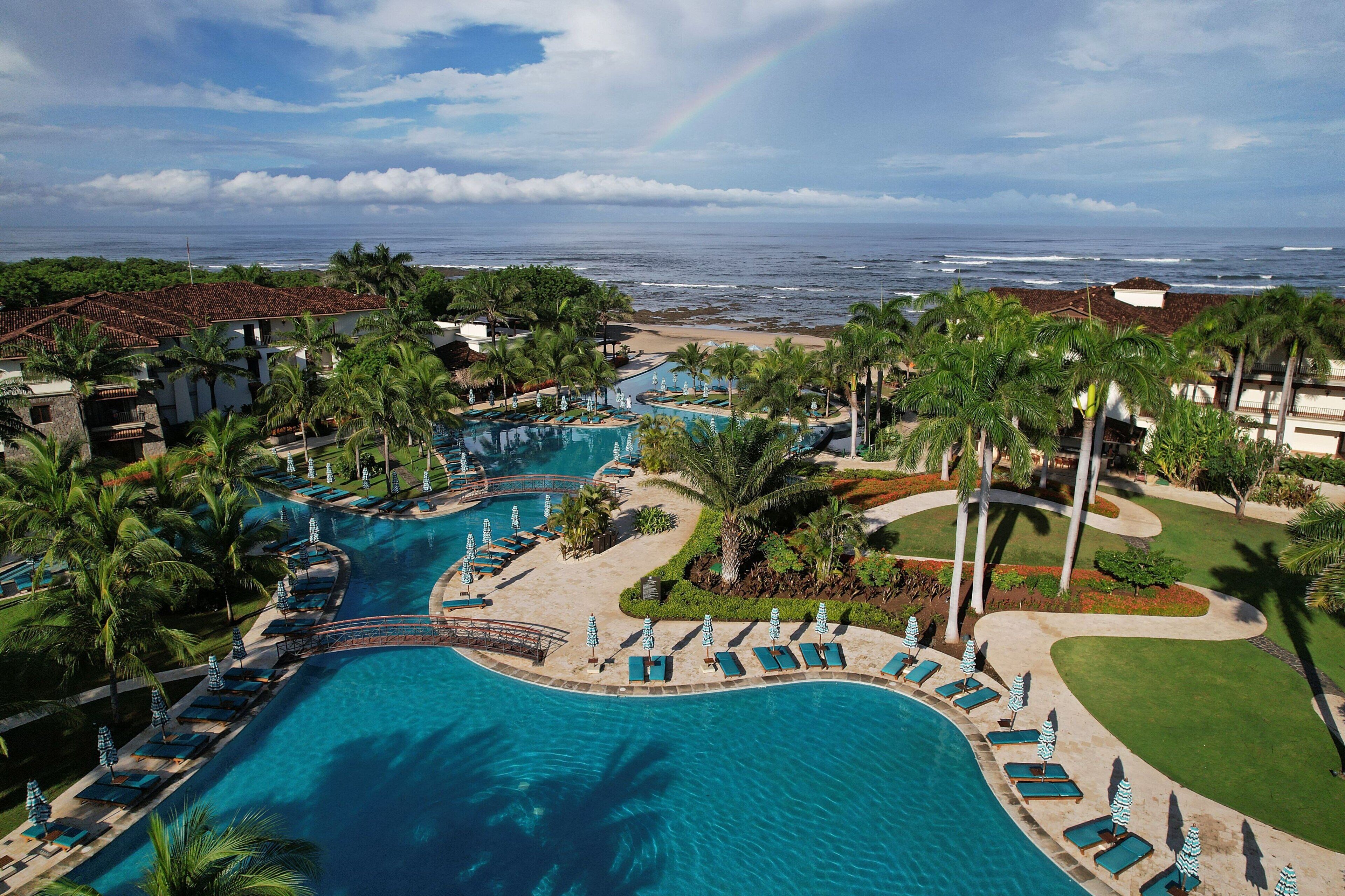 Un resort con una grande piscina, palme e vista sull'oceano.