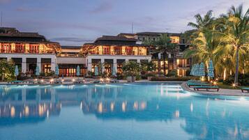 A resort with a large swimming pool, multiple buildings with balconies, and palm trees.