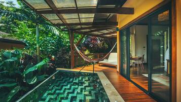 Uma piscina interior moderna com padrão geométrico de azulejos, rodeada por plantas tropicais exuberantes e uma rede.
