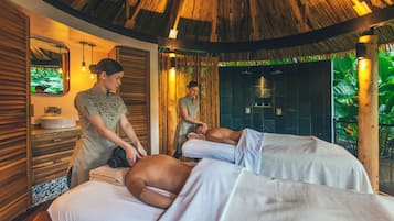 Ein Wellnessraum mit Holzwänden, einem Reetdach und zwei Massagetischen.