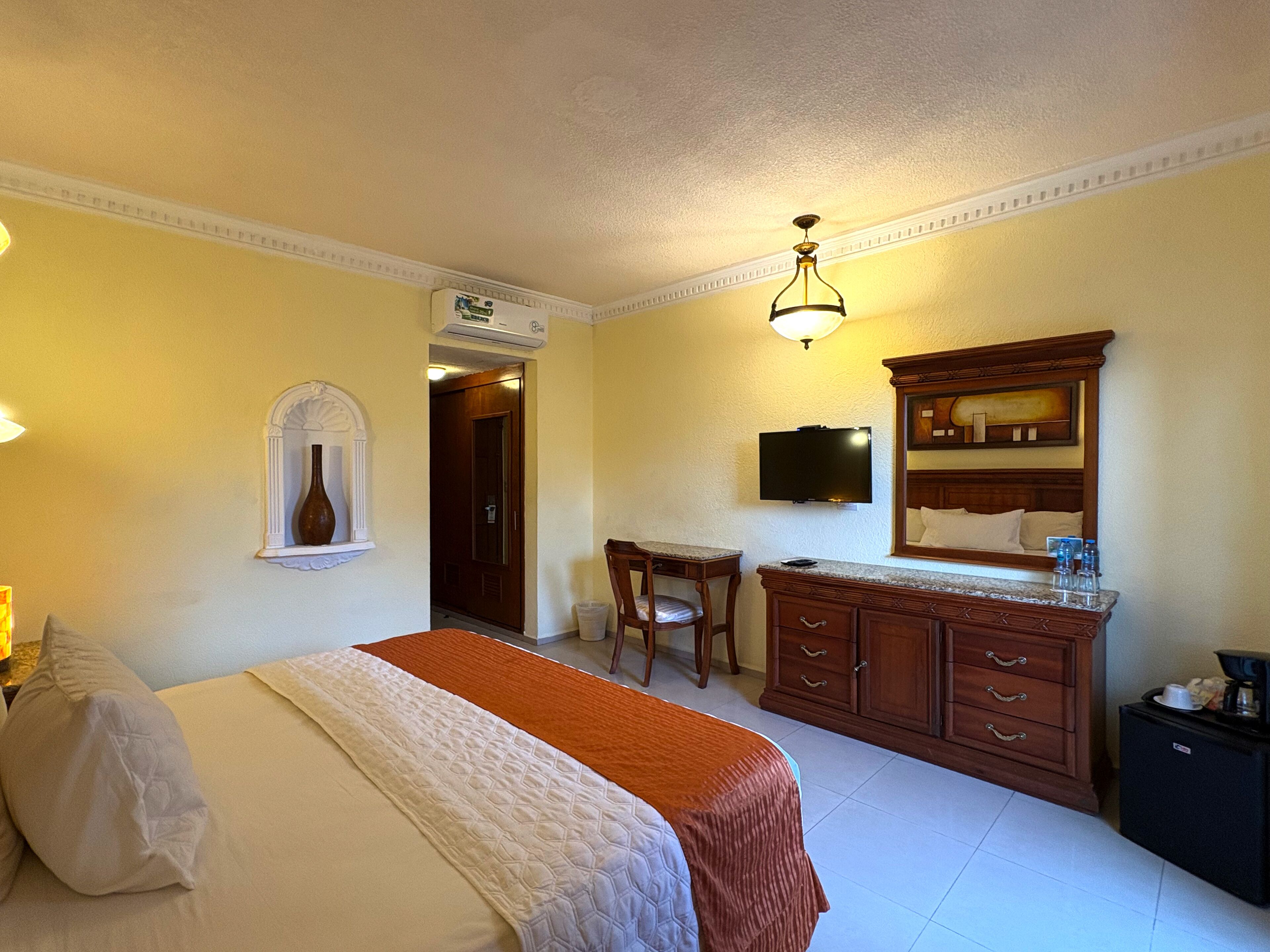 A hotel room with a bed, a desk, a dresser, a television, and a mirror.