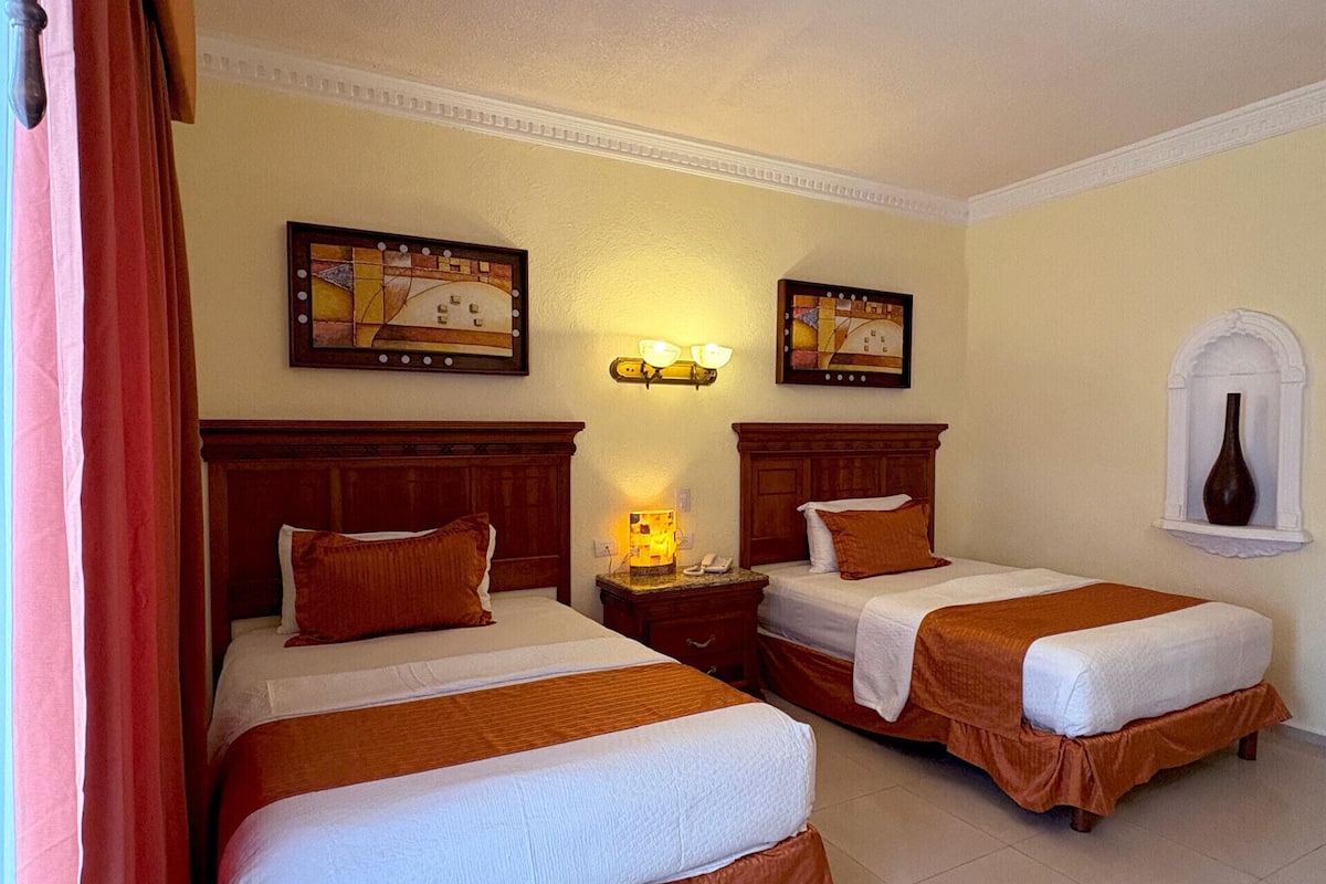 Une chambre d’hôtel avec deux lits, une table de chevet avec une lampe et des œuvres d’art accrochées au mur.