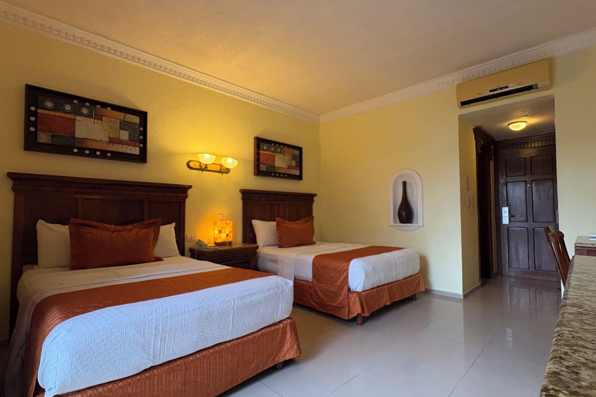 Une chambre d’hôtel avec deux lits, une table de chevet, des œuvres d’art mural et une porte donnant sur une autre pièce.
