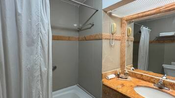 A bathroom with a bathtub, a shower, a sink with a mirror, and a telephone.