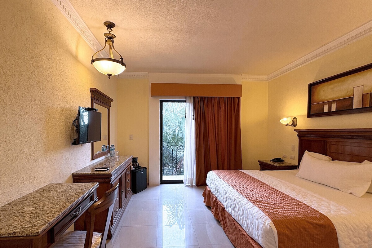 Une chambre d’hôtel équipée d’un lit, d’un bureau, d’une chaise, d’une télévision et offrant une vue sur l’extérieur, visible par la porte.