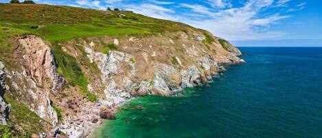 A coastal landscape with a grassy hill and rocky cliffs overlooking clear blue waters.