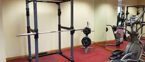 A gym with a squat rack, weight bench, and an elliptical machine.