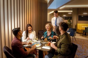 A group of people dining at a table in a modern hotel room with a striped wall and a patterned carpet. - Maldron Hotel Newlands Cross (Dublin)