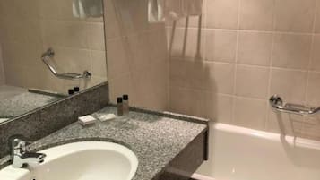 A bathroom with a white sink, a mirror, a towel rack with folded towels, and a bathtub.