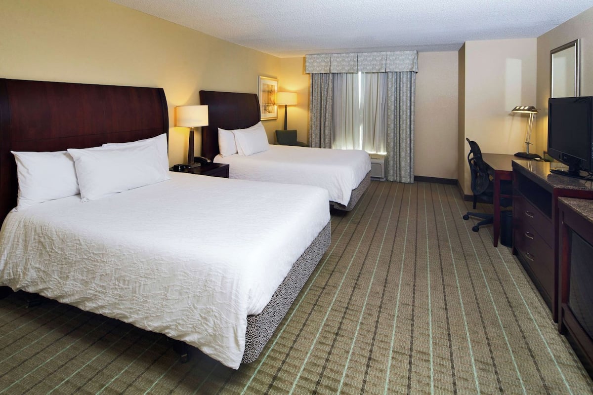A hotel room with two beds, a desk, a television, and a window with curtains.