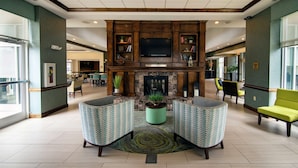 A spacious lobby with a fireplace, seating area, and a television mounted on the wall. - Hilton Garden Inn Valdosta (Valdosta)