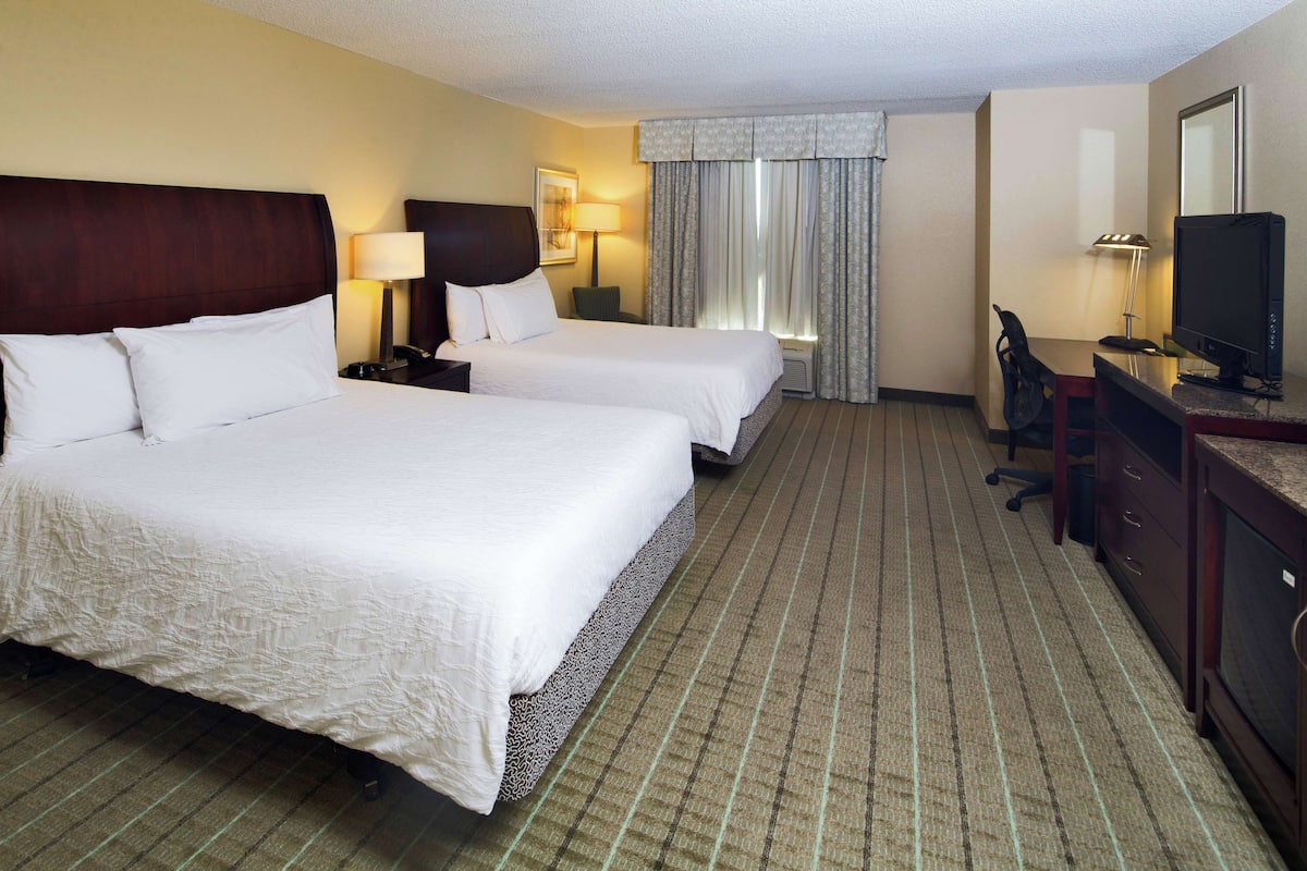 A hotel room with two beds, a desk, a chair, a television, and a window with curtains.