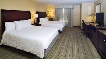 A hotel room with two beds, a desk, a chair, a television, and a window with curtains.