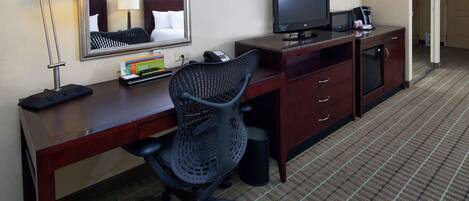 A hotel room with a desk, a chair, a television, a telephone, and a microwave.