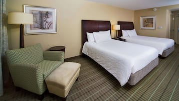 A hotel room with two beds, a chair, a small table, and a lamp.