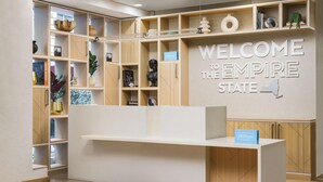 A reception desk with a 'Welcome to the Empire State' sign, wooden shelving with various items, and a 'Hilton Honors' sign. - Hampton Inn Manhattan-35th St/Empire State Bldg (New York)