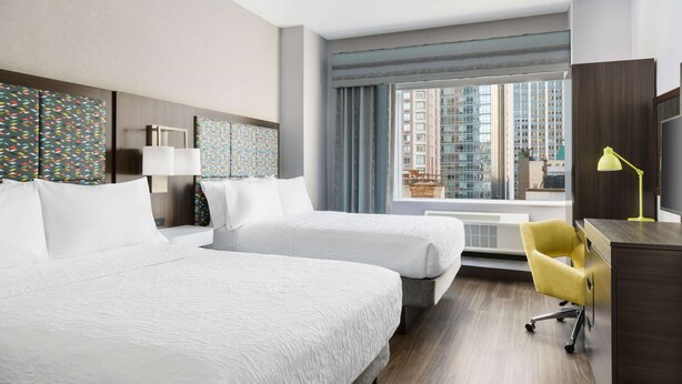 A hotel room with two beds, a desk with a chair, a window with a view of buildings, and a lamp. - Hampton Inn Manhattan-35th St/Empire State Bldg (New York)