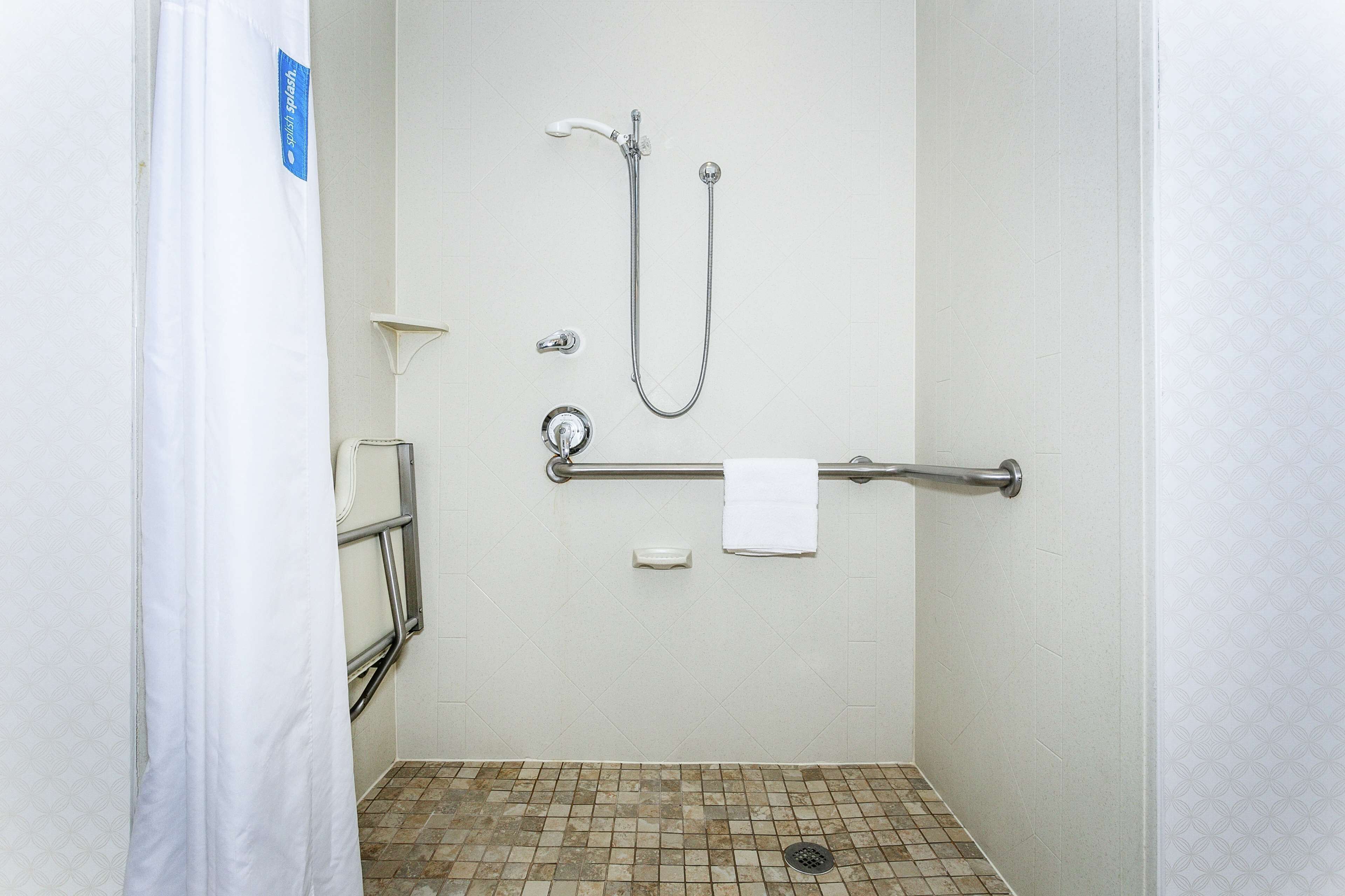 A shower area with a grab bar, a handheld showerhead, and a towel rack.
