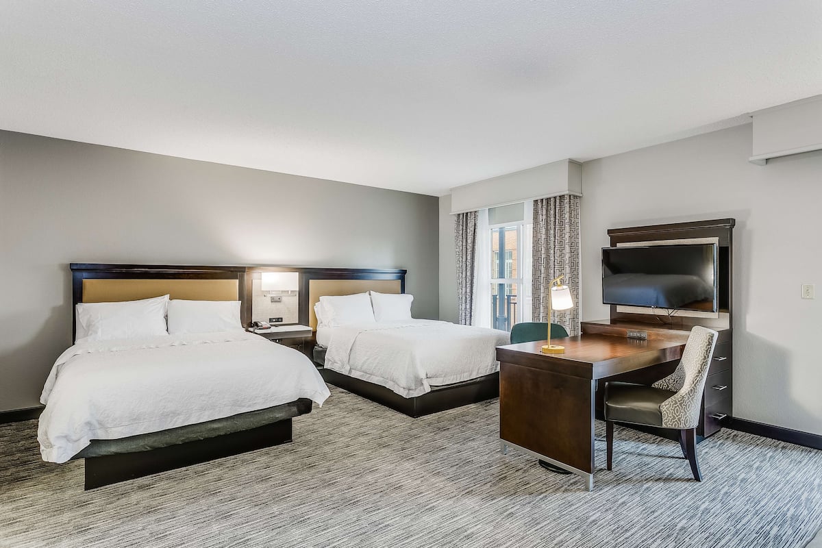 A hotel room with two beds, a desk, a chair, a TV, and a window with curtains.
