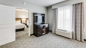 Een hotelkamer met een bed, een donker houten dressoir, een flatscreen televisie, een raam met behang en een wandairconditioning.