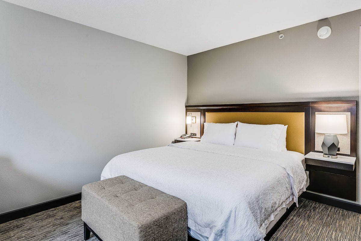 A hotel room with a large bed, a nightstand with a lamp, and a small bench.
