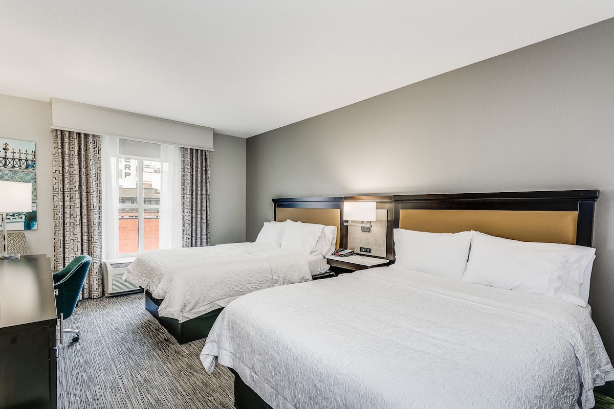 A hotel room with two beds, a desk, a chair, and a window with curtains.