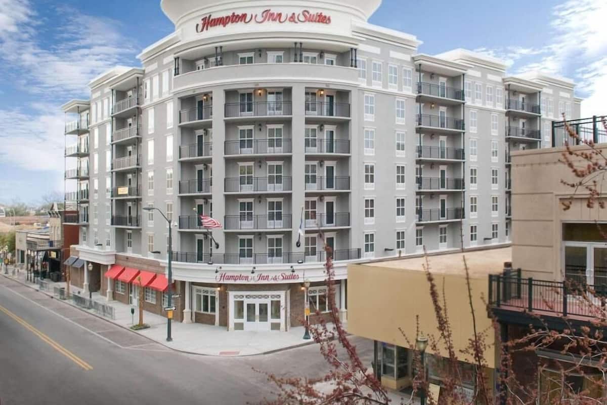 A multi-story Hampton Inn & Suites hotel with a central entrance, balconies, and a clear sky.