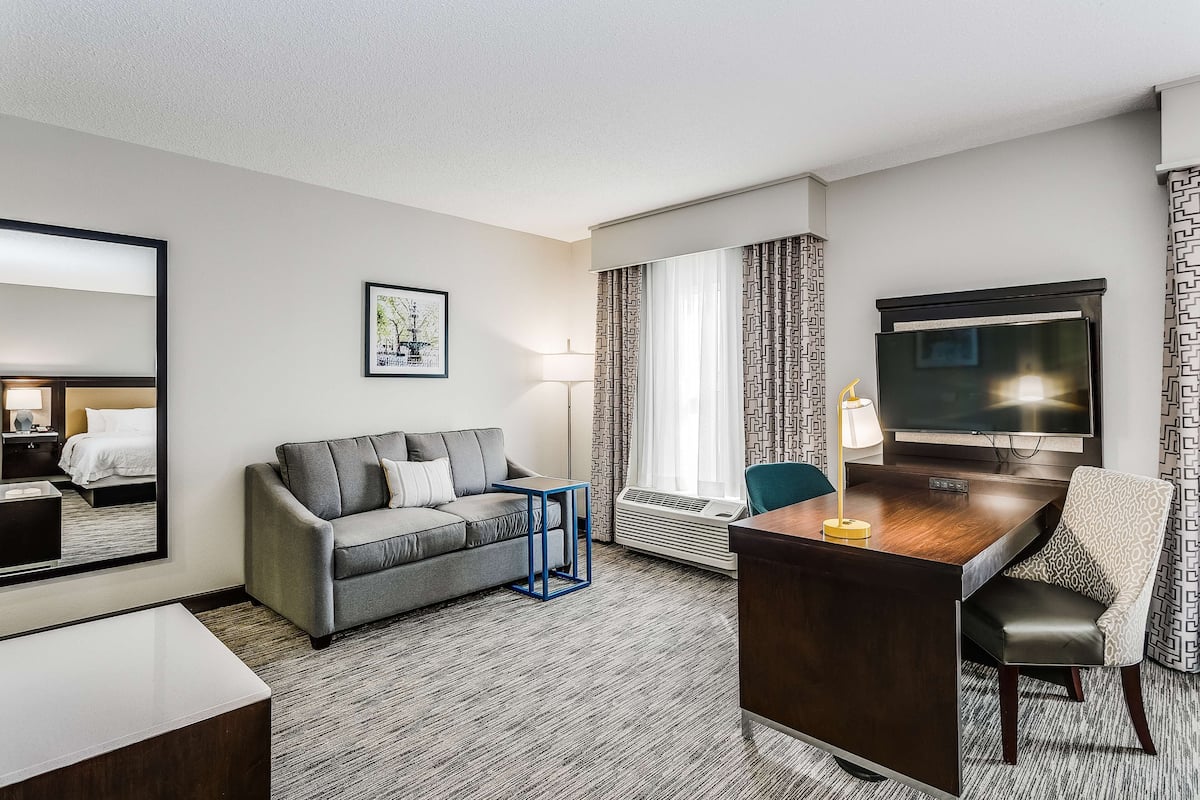 A hotel room with a grey sofa, a wooden desk, a television, and a patterned curtain.