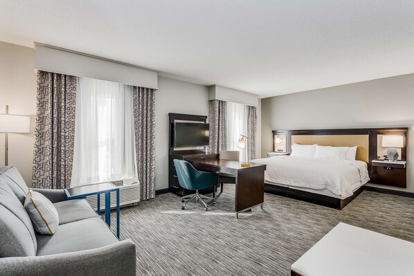 A hotel room with a bed, a desk, a chair, a sofa, and a TV. - Hampton Inn & Suites Mobile- Downtown Historic District (Mobile)