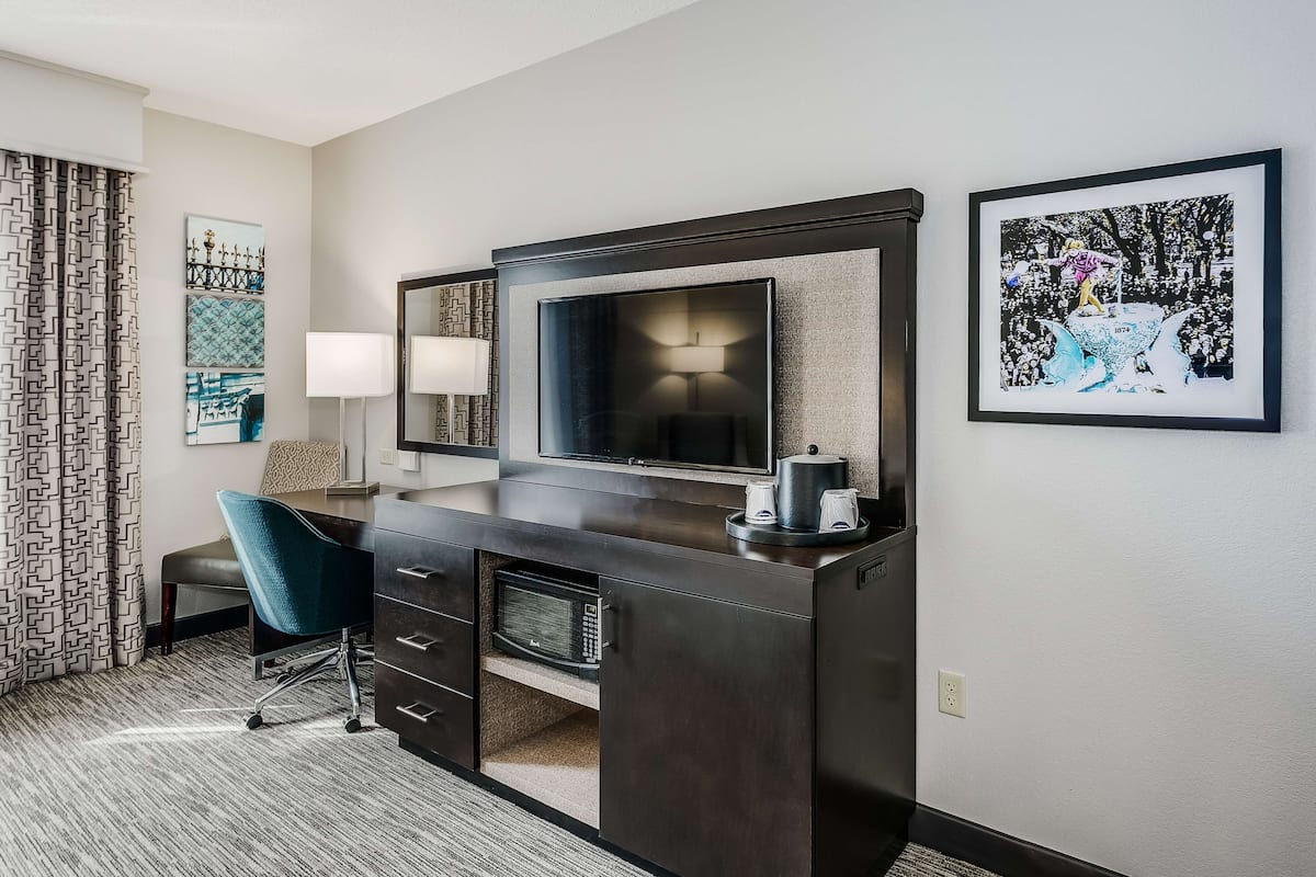 A hotel room with a dark wooden desk, a flat-screen TV, a blue chair, and a framed picture on the wall.