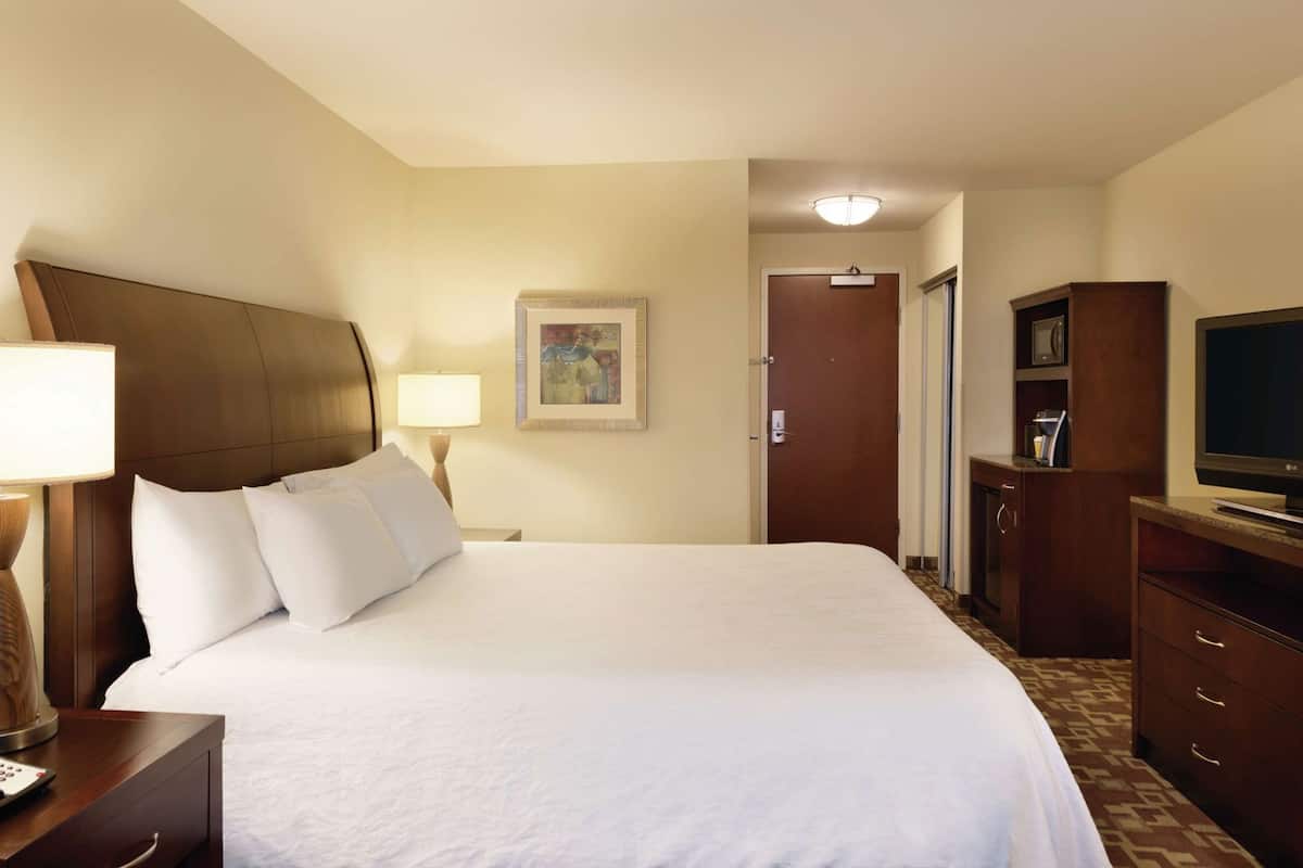 Une chambre d’hôtel avec un grand lit, un bureau avec une lampe, une télévision et une porte donnant sur une autre pièce.
