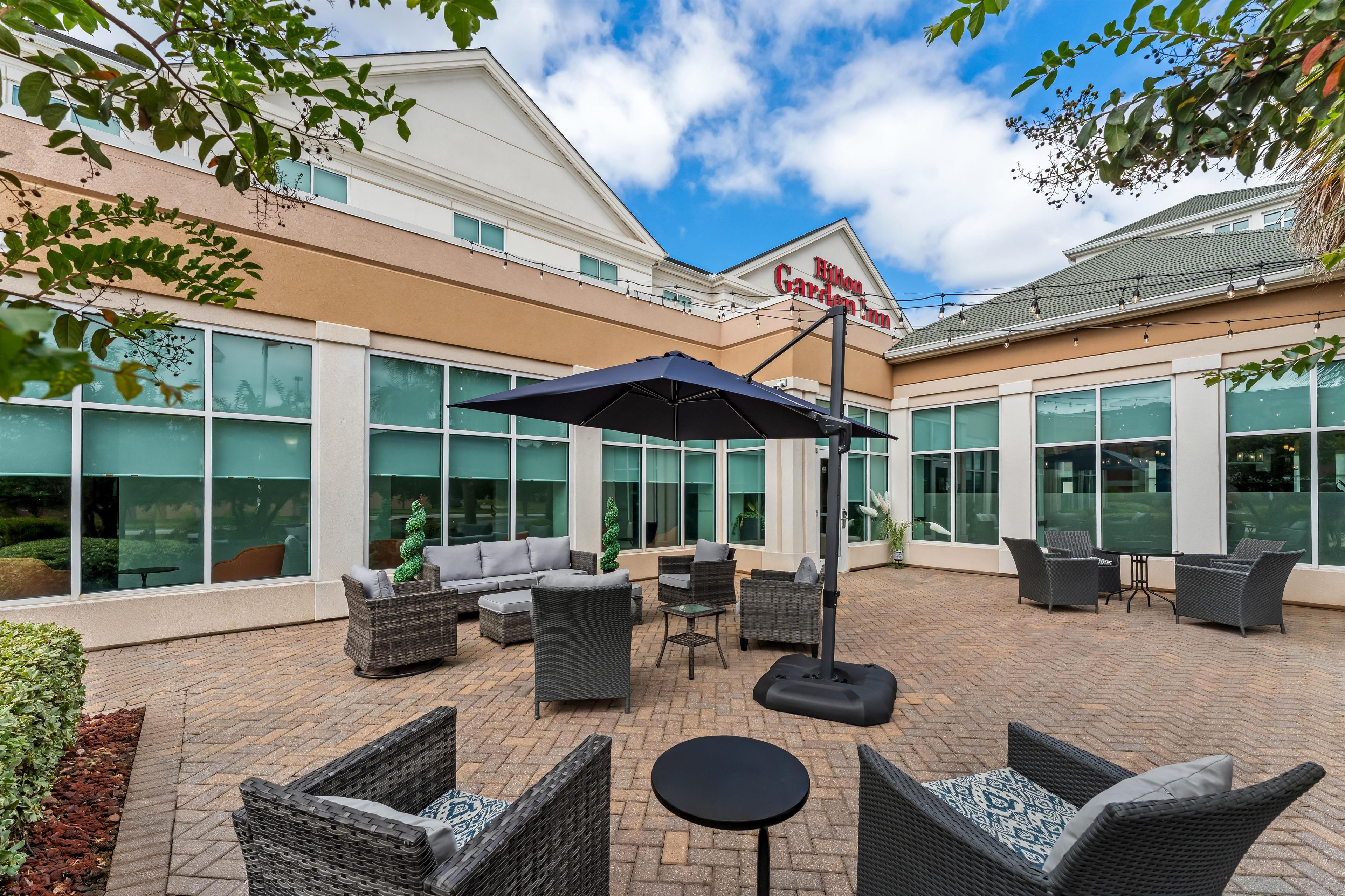 A hotel patio with outdoor seating, large windows, and a clear sky.