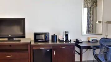 A hotel room with a TV, microwave, coffee maker, desk, chair, and a small refrigerator.