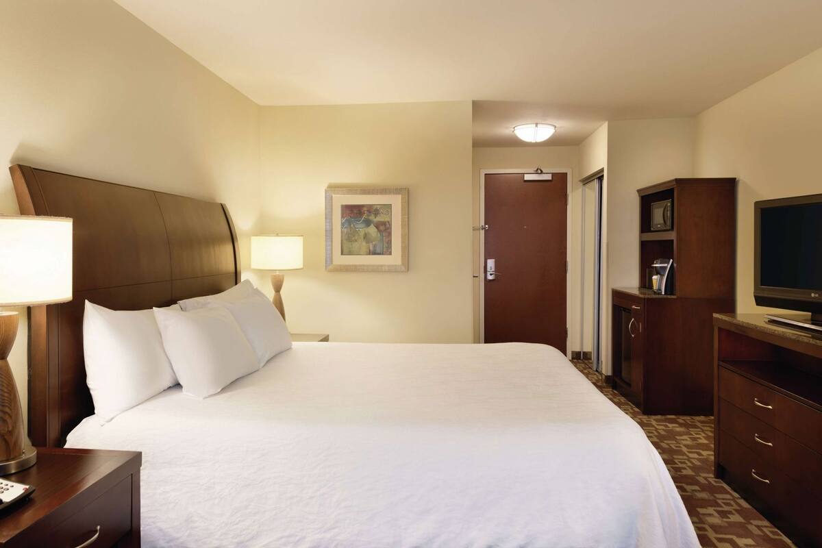 Une chambre d’hôtel avec un grand lit, un bureau avec une lampe, une télévision et une porte donnant sur une autre pièce.