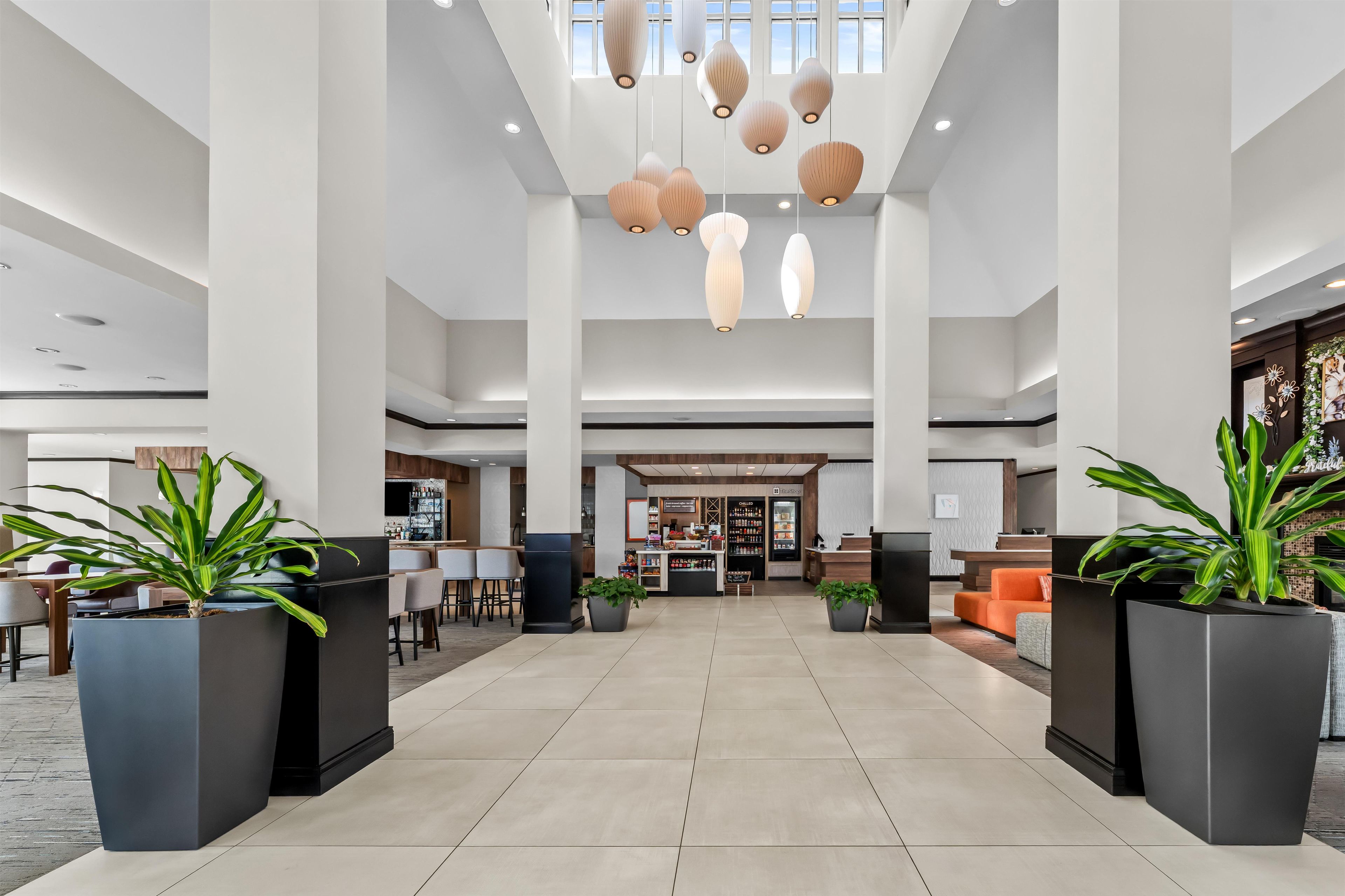 Eine großzügige Lobby mit hoher Decke, moderner Pendelleuchten und einer zentralen Rezeption.