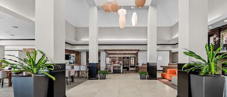 A spacious lobby with a high ceiling, modern pendant lighting, and a central reception desk.