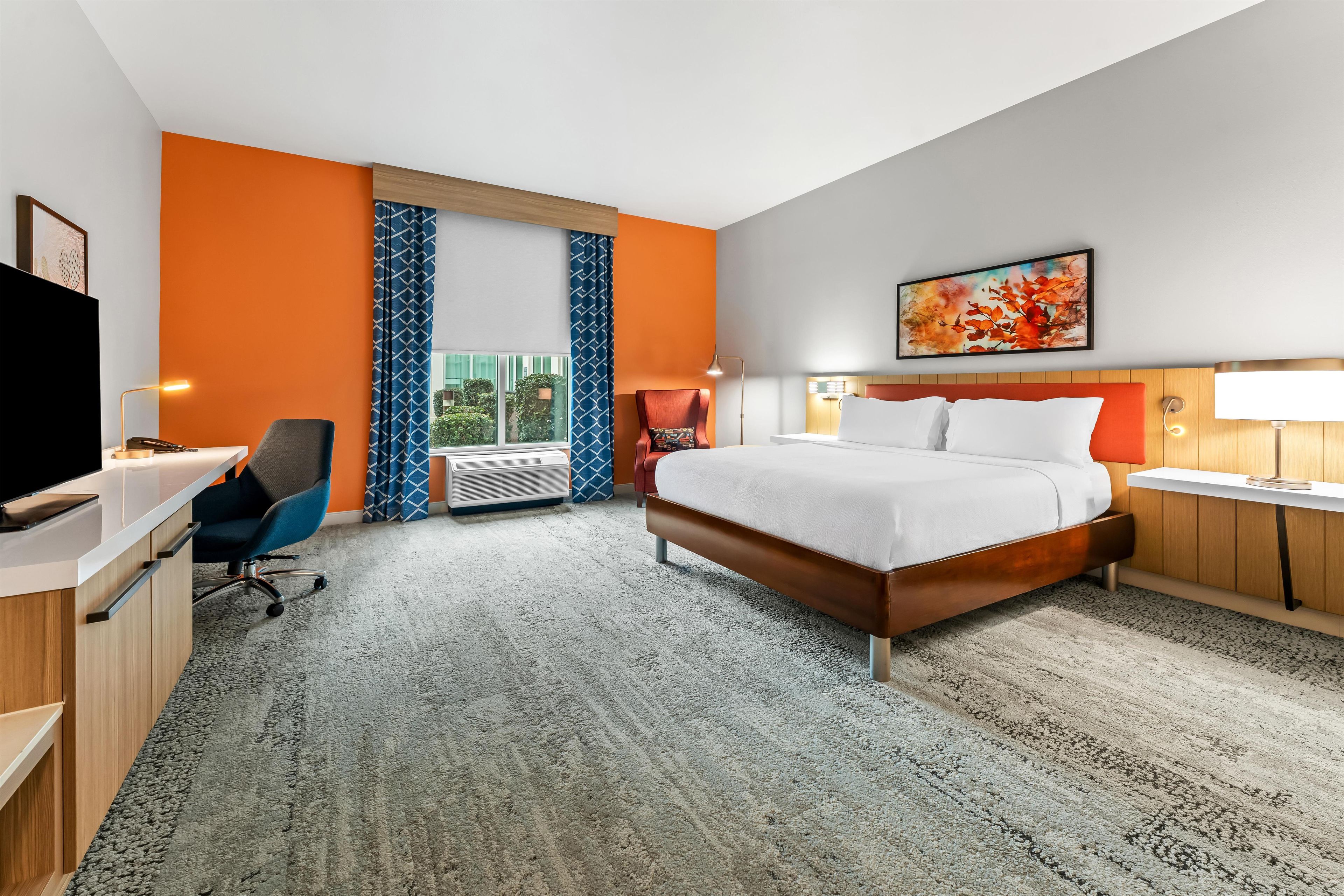 Une chambre d’hôtel avec un lit, un bureau, une chaise et une grande fenêtre.