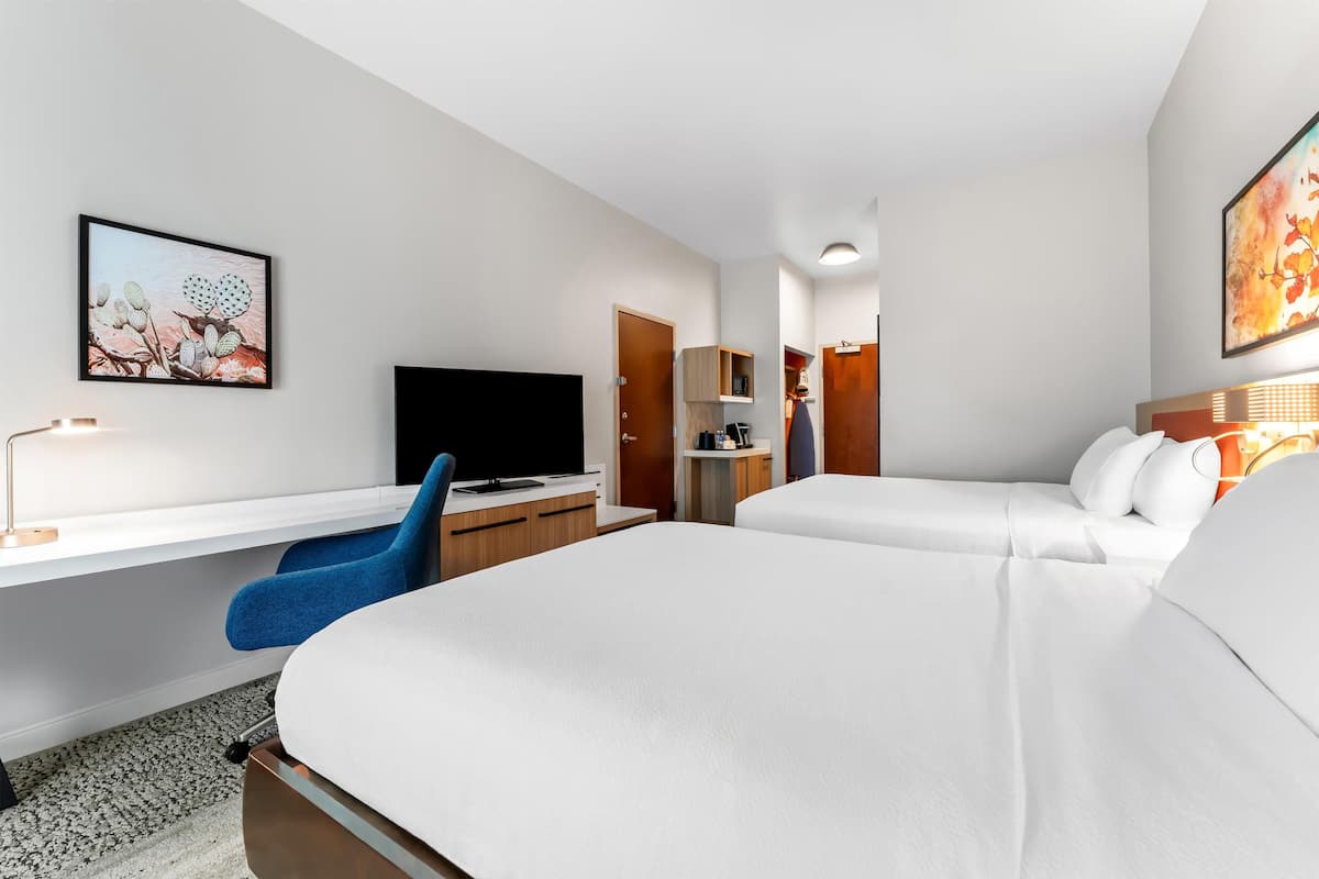 Une chambre d’hôtel moderne équipée d’un lit, d’un bureau, d’une chaise, d’une télévision et ornée d’œuvres d’art sur les murs.