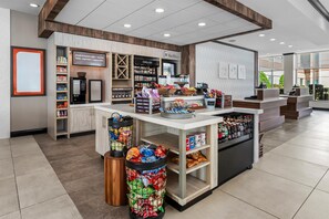 A modern coffee shop interior with a coffee machine, shelves stocked with snacks, and a counter with a variety of beverages.
