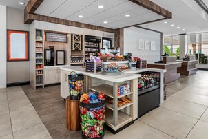 Interior moderno de una cafetería con una máquina de café, estantes llenos de bocadillos y una barra con diversas bebidas.