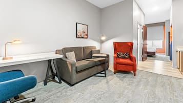 A modern living room with a white desk, a grey sofa, a blue chair, and a red armchair.