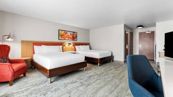 A hotel room with two beds, a desk, a chair, a lamp, and a painting on the wall.