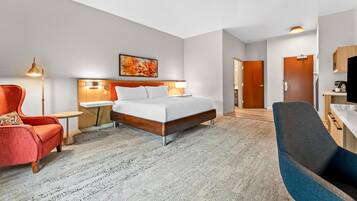 A hotel room with a bed, a desk, a chair, a lamp, and a painting on the wall.