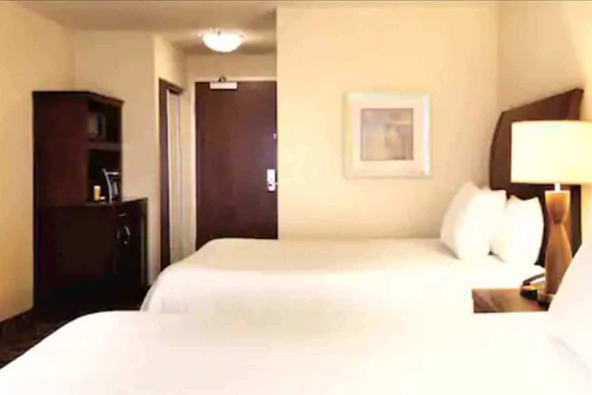 Une chambre d’hôtel avec deux lits, un bureau, une armoire et une porte.